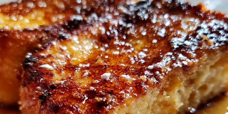 Golden brown Crème Brûlée French Toast with caramelized sugar crust being torched, served on white plates with fresh raspberries and blueberries