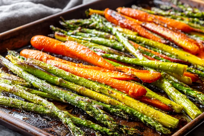 Close-up of vegetables being tossed in a clear glass bowl with honey glaze, showing the glossy coating technique and chef's hands mixing