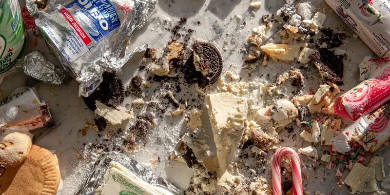 A stunning whole no-bake peppermint Oreo cheesecake on a black cake stand, showing thick creamy white filling topped with swirls of whipped cream, crushed red and white candy canes, and dark Oreo cookie crumbles against a soft gray marble background