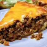 A delicious slice of Taco Pie topped with cheese, lettuce, and salsa on a plate.