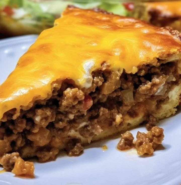A delicious slice of Taco Pie topped with cheese, lettuce, and salsa on a plate.