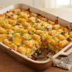A close-up of a baked Tater Tot Sausage Breakfast Casserole in a 9x13 baking dish, showing layers of tots, sausage, and melted cheese.