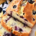 Slice of blueberry lemon pound cake loaf on a white plate with fresh blueberries