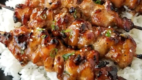 Grilled teriyaki chicken skewers on a plate garnished with green onions